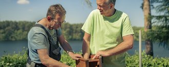 Haus am See 2 Personen die an einem Vogelhaus arbeiten.